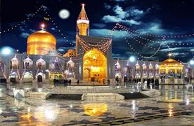 تصویری از صحنِ چراغانی‌شده حرم امام رضا در شب که گنبد و گلدسته طلایی در آن دیده می‌شود. 